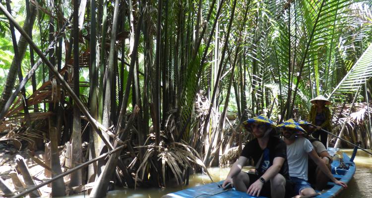 Turistas en una embarcación tradicional bajo la densa cubierta de un bosque de palmeras.