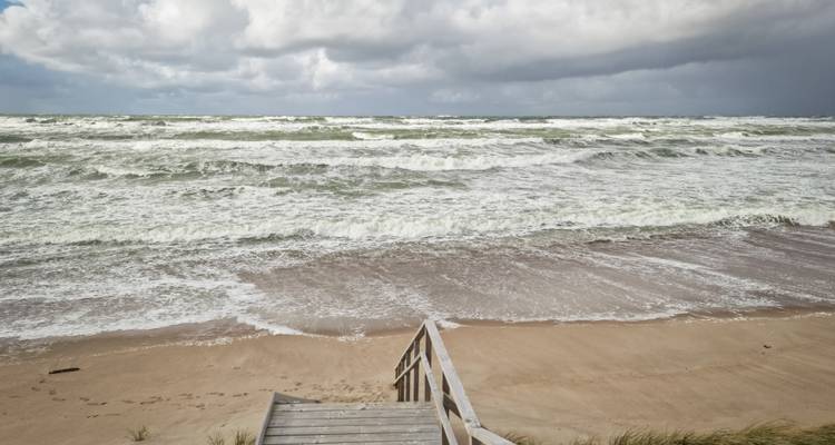 Golven die neerstorten op een zanderig strand onder bewolkte luchten.