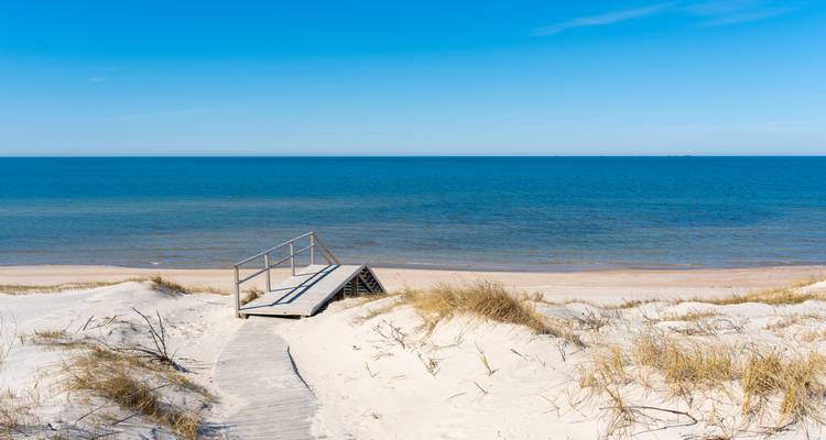 Houten wandelpad dat leidt naar een rustig strand met heldere luchten.