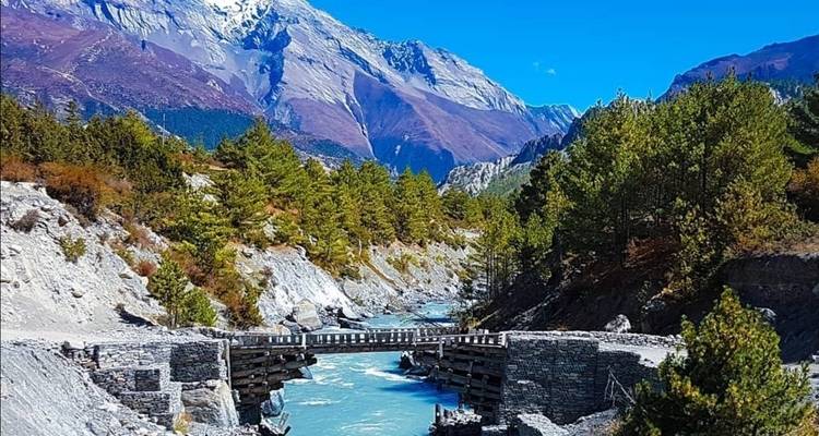 Kristalheldere rivier onder een brug met bergen op de achtergrond.