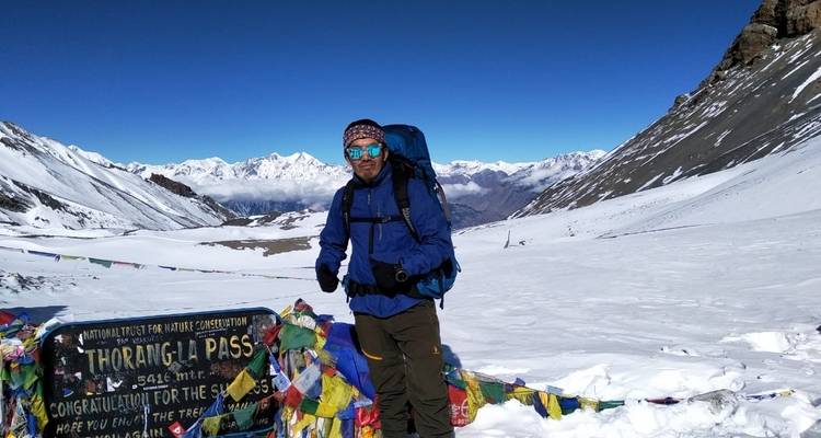 Person am Thorong La Pass mit Schnee und Gebetsfahnen.