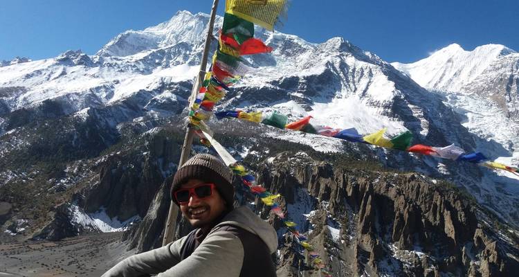 Person mit Sonnenbrille in der Nähe bunter Gebetsfahnen mit schneebedeckten Bergen.