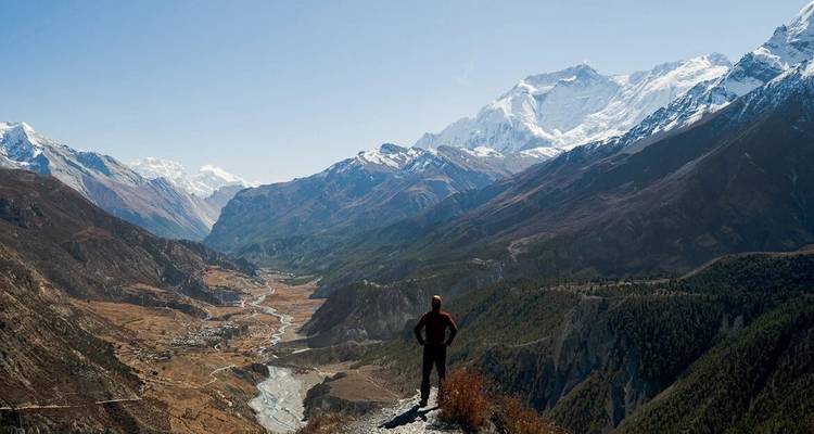 Person, die auf einer Klippe steht und auf ein Bergtal blickt.