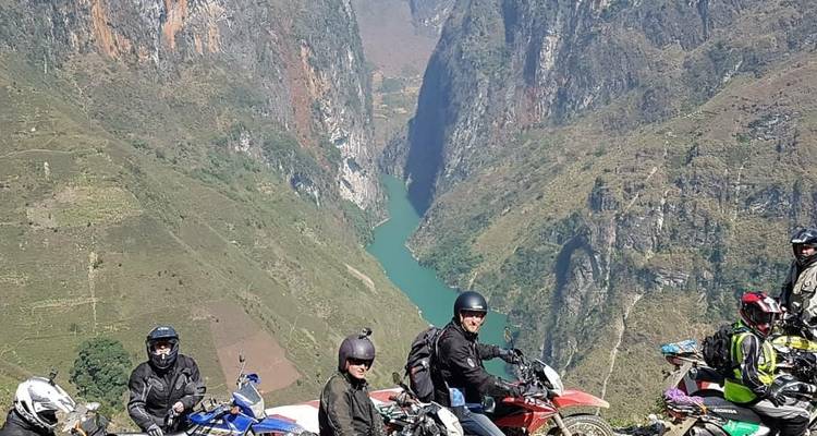 Motorradfahrer an einem malerischen Aussichtspunkt mit einer tiefen Schlucht und einem Fluss darunter.