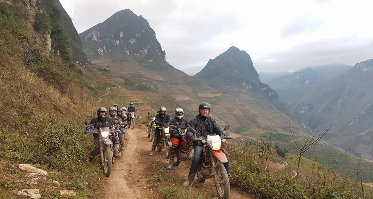 Motorradfahrer, die einen Erdweg zwischen hohen Bergen befahren.