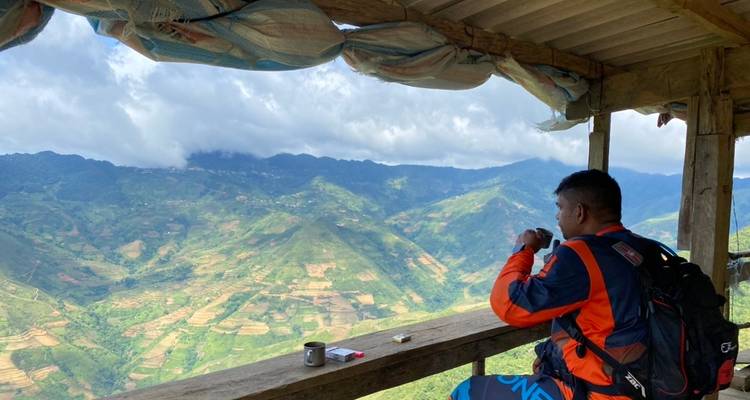 Person, die auf einem hölzernen Balkon sitzt und auf ein weites Tal blickt.