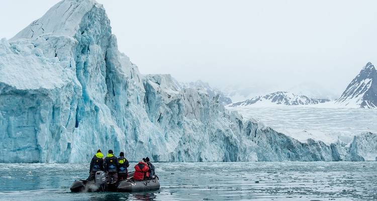 Petit bateau pneumatique gonflable avec des explorateurs regroupés s'approchant de parois glaciaires bleues imposantes dans des eaux glacées.