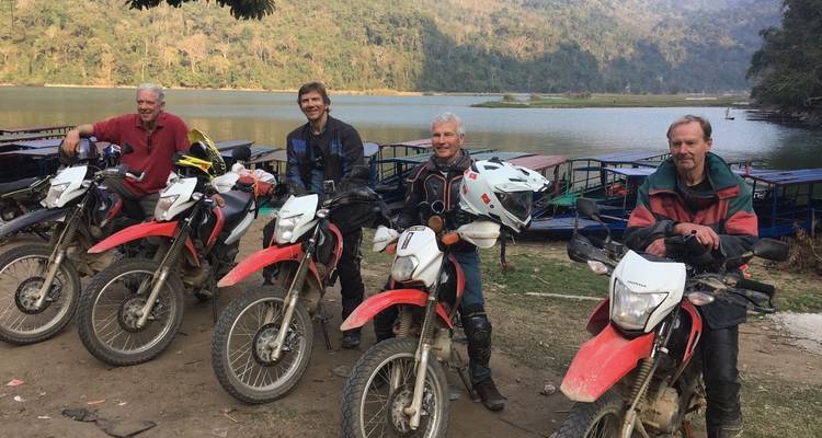 Groupe d'hommes avec des motos au bord d'un lac.