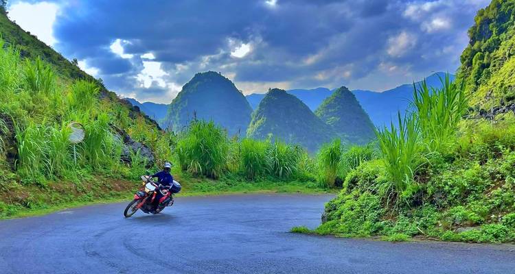 Motorradfahrer fährt entlang einer Kurve mit üppig grünen Hügeln im Hintergrund.