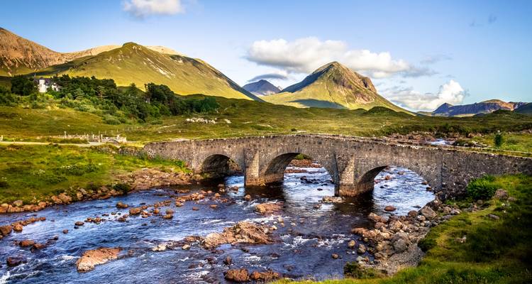 Puente de piedra antiguo sobre un río en un paisaje montañoso.