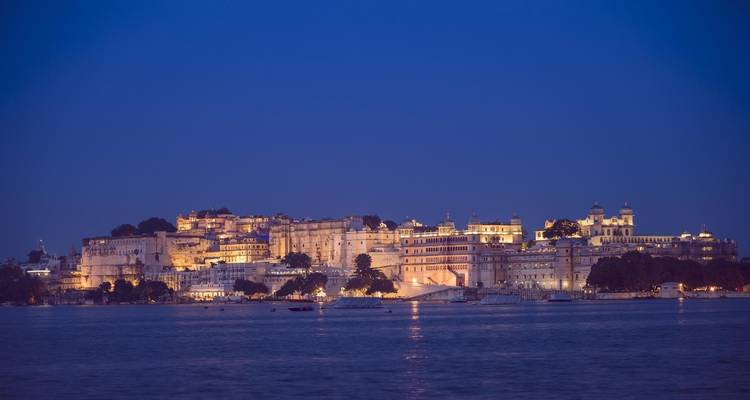 Luces de la ciudad reflejándose en un lago con vista a un palacio.