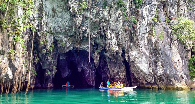 Turistas explorando una cueva en bote sobre agua verde cristalina.