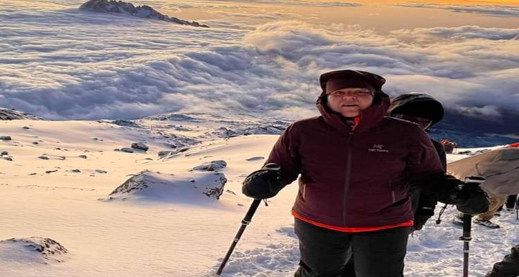 Eine Person in Winterausrüstung auf einem schneebedeckten Berg mit Wolkendecke darunter.