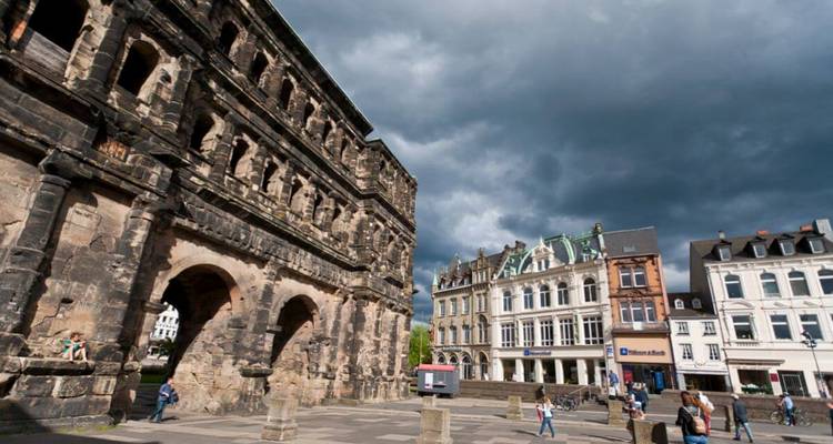 Porte romaine antique avec des bâtiments modernes sous un ciel nuageux.