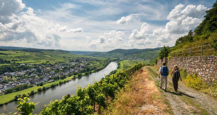Deux randonneurs marchant le long d'un sentier surplombant une rivière et un village.