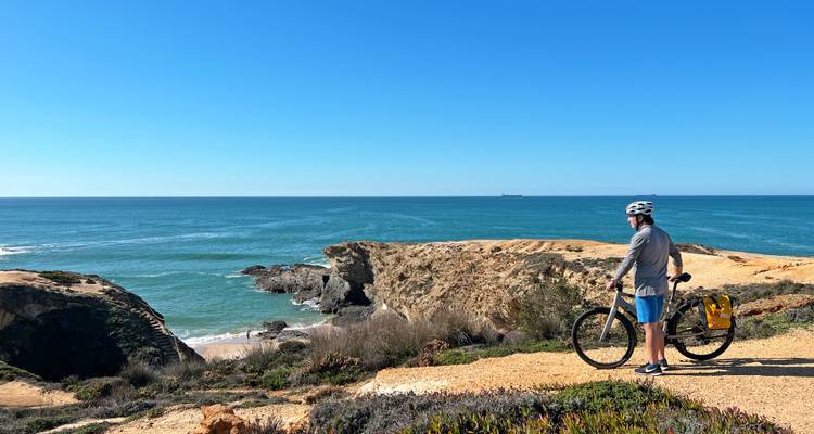 Cycliste casqué fait une pause sur un sentier de falaise côtière surplombant un vaste océan bleu et un littoral accidenté.