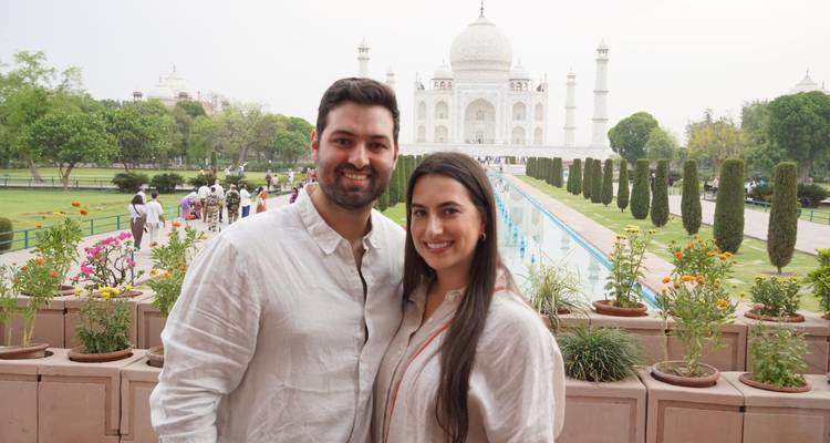 Pareja sonriente posando frente al Taj Mahal con su estanque reflectante.