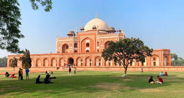 La Tumba de Humayun con visitantes relajándose en el césped bajo un cielo azul despejado.