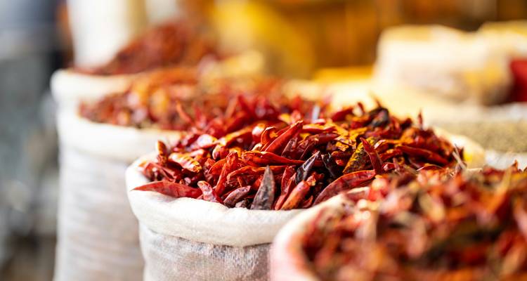 Sacos de arpillera desbordantes de chiles rojos secos en un mercado bullicioso.