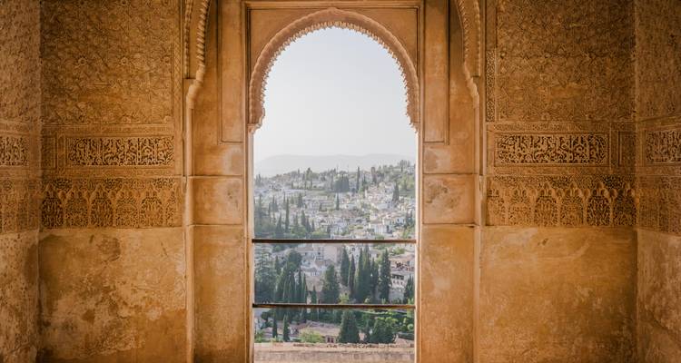Ventana de arco morisco intrincado de la Alhambra que enmarca una vista del paisaje urbano de Granada.