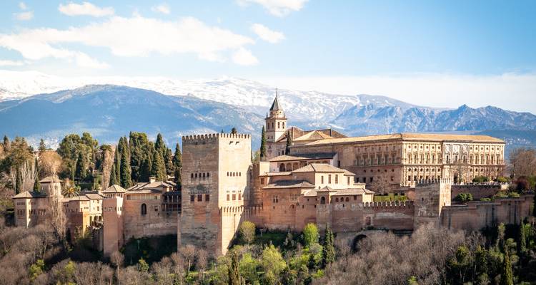 Vista expansiva del complejo palaciego de la Alhambra recortado contra las montañas de Sierra Nevada cubiertas de nieve.