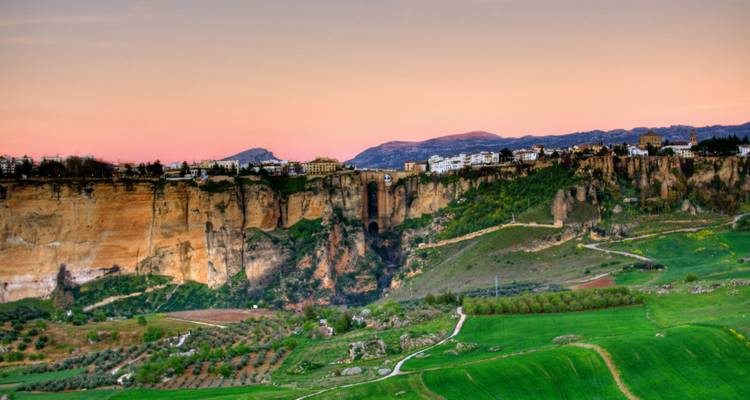 El brillo del atardecer sobre los acantilados dramáticos y los campos verdes que rodean la garganta profunda de Ronda.