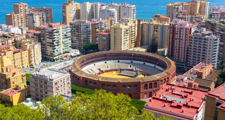 Vista aérea de la plaza de toros circular de Málaga rodeada de coloridos edificios de gran altura y el mar azul.