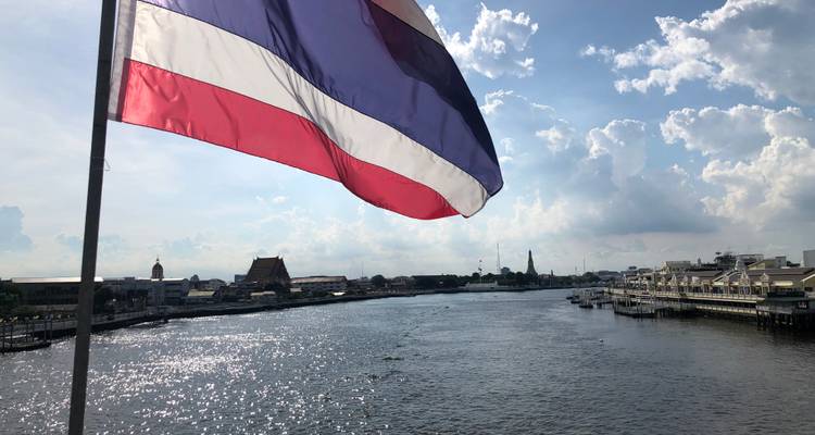 Thai flag waving over a wide river with cloudy sky.