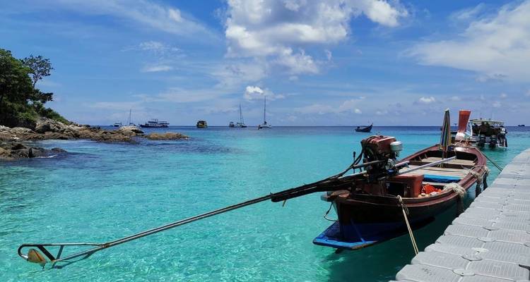Beach with clear turquoise water and a longtail boat docked.