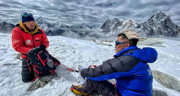 Dos escaladores tomando un descanso en una zona montañosa cubierta de nieve.