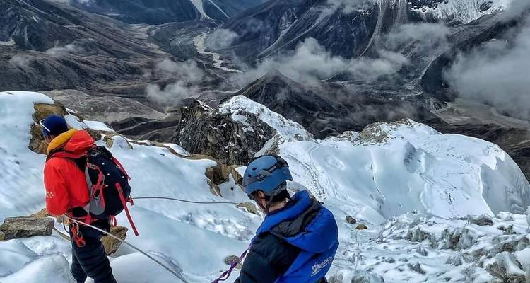 Two climbers descending a snowy mountain ridge with valley views.