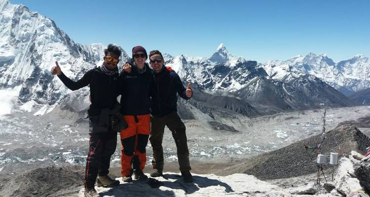 Three people posing on a mountain with snow peaks in the background.