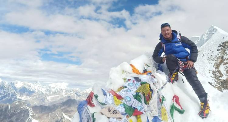 Persoon in klimuitrusting op de top van een met sneeuw bedekte bergpiek.