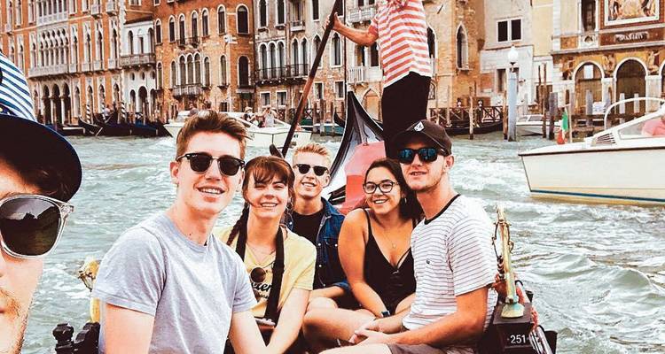 Selfie de amigos sentados en una góndola navegando por el concurrido Gran Canal de Venecia con fachadas históricas detrás de ellos