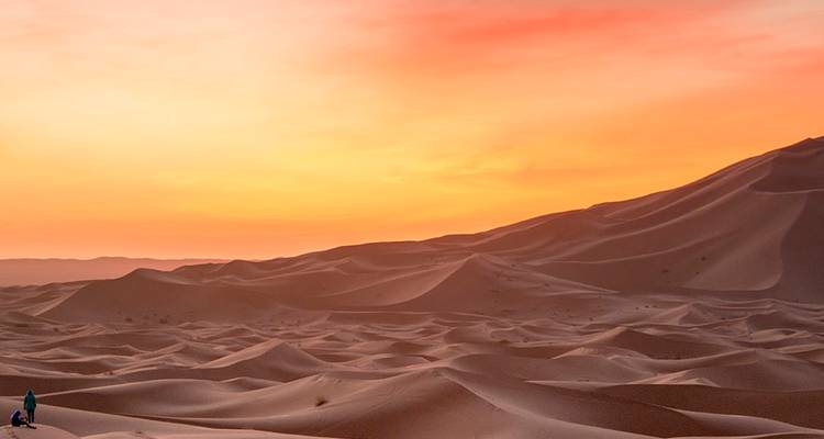 Las inmensas dunas de arena ondulante brillan en naranja bajo un cielo de salida del sol dramático