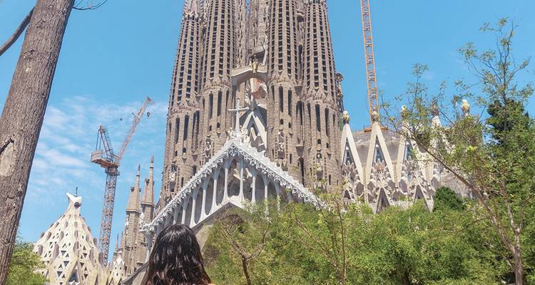 Achteraanzicht van een reiziger die de oprijzende torenspitsen van de Sagrada Familia bewondert tegen een wolkenloze hemel.