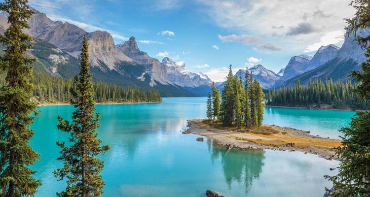 Un lac turquoise entoure un îlot couronné d'arbres encadré par des pics escarpés saupoudrés de neige.