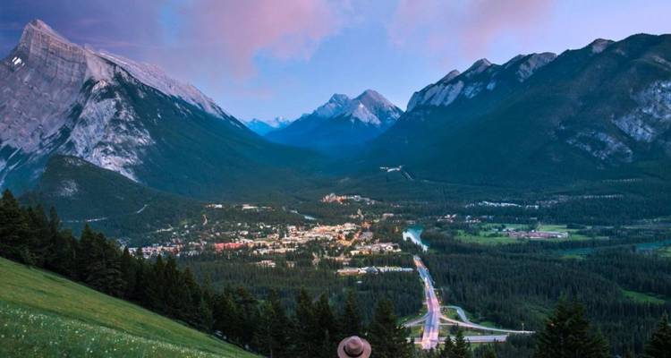 Un voyageur portant un chapeau à large bord contemple la ville de Banff nichée dans une vallée des Rocheuses majestueuse au crépuscule.