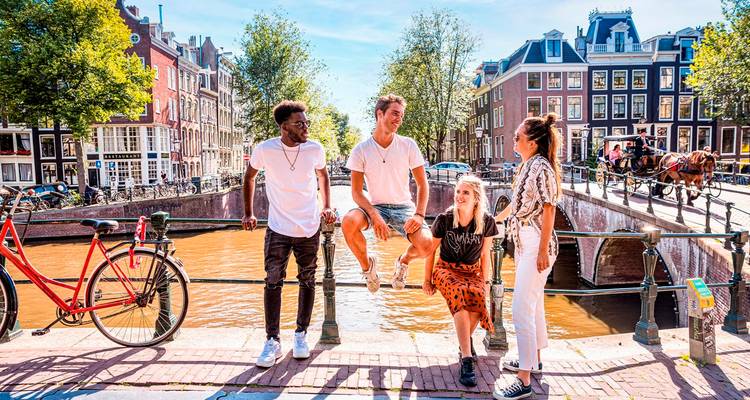 Gruppe von Menschen, die an einem Kanal stehen, mit Gebäuden und einem roten Fahrrad in der Nähe.