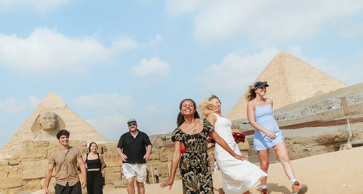 Voyageurs souriants et posant près des Grandes Pyramides de Gizeh avec un ciel bleu au-dessus.