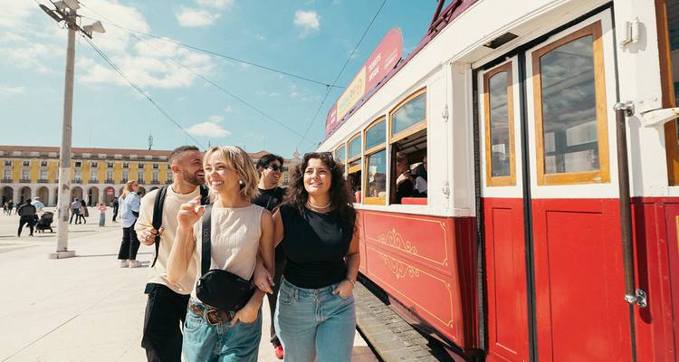 Groep vrienden die lachen naast een klassieke rood-gele stadstram op een zonnig plein