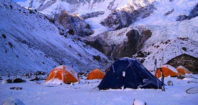 Met sneeuw bedekte tenten bij een bergbasiskamp met een gletsjer op de achtergrond.