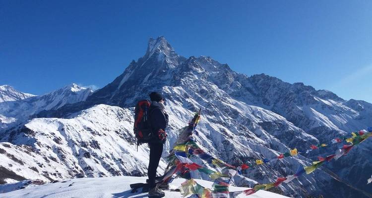 Wanderer blickt auf schneebedeckte Berge mit Gebetsfahnen im Vordergrund.