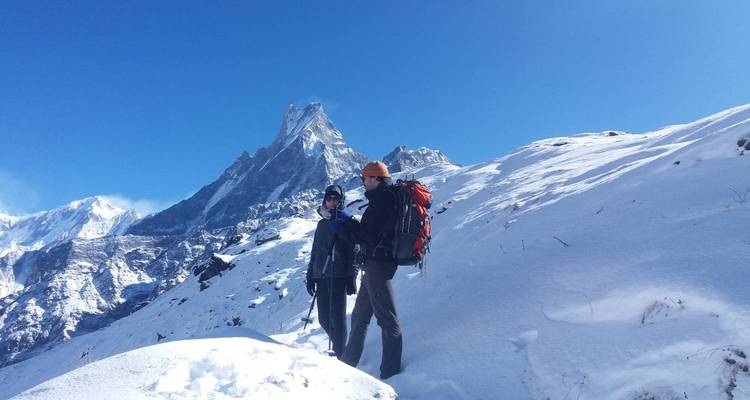 Zwei Wanderer in schneebedeckten Bergen mit einem markanten Gipfel im Hintergrund.