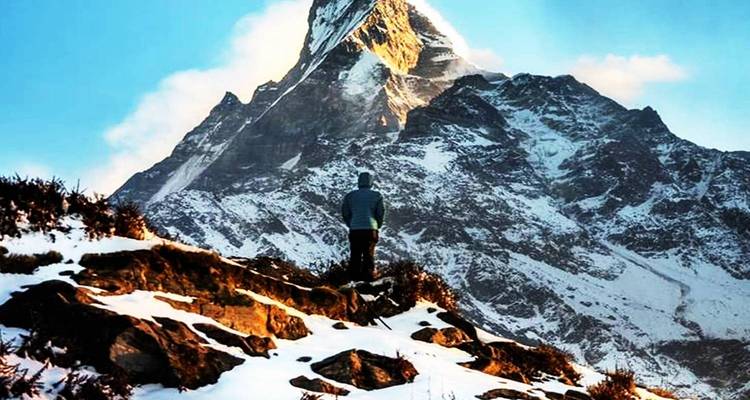 Einzelne Person, die am Fuß eines schneebedeckten Berges steht und nach oben blickt.