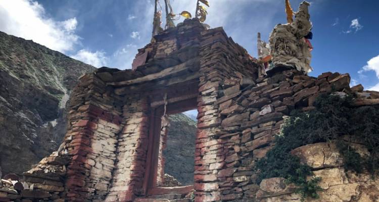 Ruinierte Steinstruktur mit Gebetsfahnen in bergiger Region.