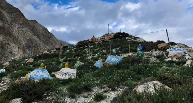Bemalte Felsbrocken und Gebetsfahnen in einer Berglandschaft.