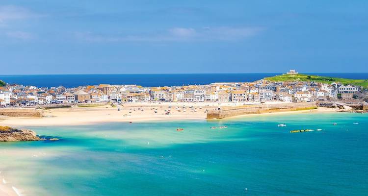 Ville côtière colorée et plage de sable en croissant encadrée par des eaux turquoise et un ciel bleu.