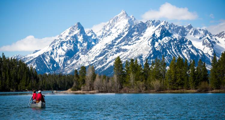Canoeists on a lake with towering snow-capped mountains in the background.