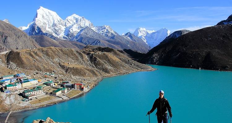 Wandelaar die uitkijkt over een turquoise meer en besneeuwde toppen.